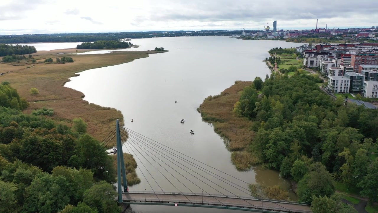 Ampia ripresa aerea dello skyline urbano di Helsinki con i grattacieli di Kalasatama e la centrale elettrica di Hanasaari attraverso la baia di Vanhankaupunginselkä. Paesaggio costiero scenografico sotto un cielo cupo e nuvoloso