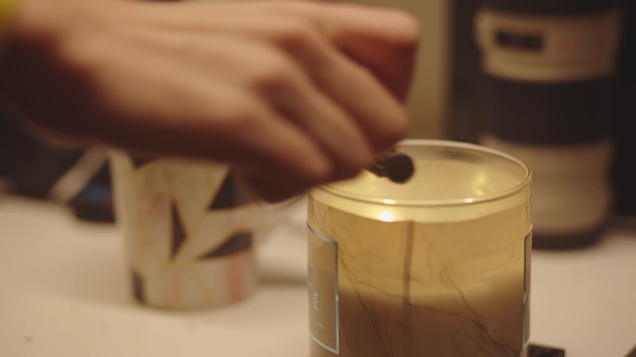 la mano usa un encendedor para encender una vela aromática en un frasco de vidrio - cerrar