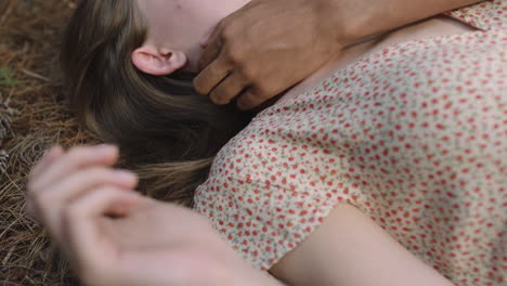 young man touching womans face with hand gently caressing showing affection teenage couple lying on ground in forest woods