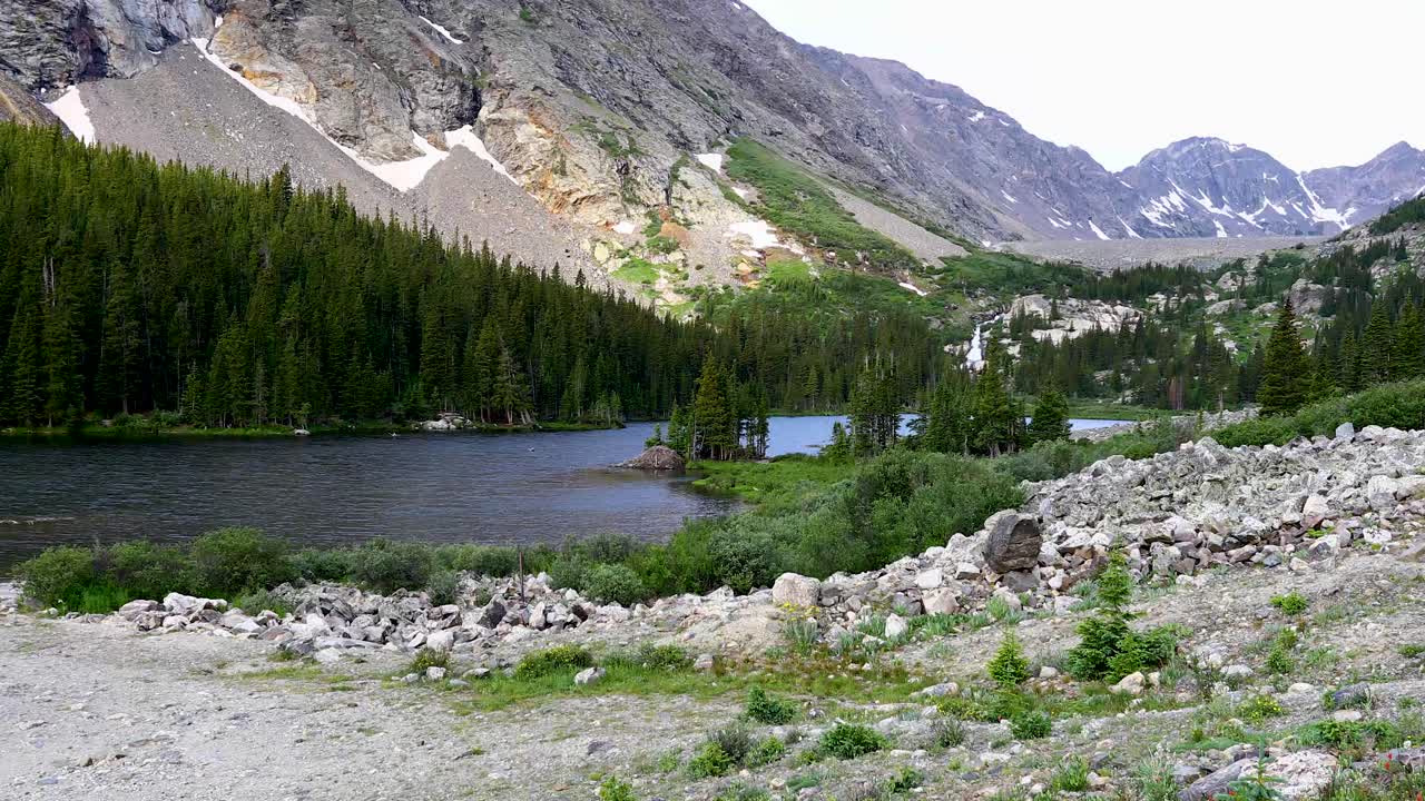 Static video of Lower Blue Lake in Breckenridge Colorado. Trees and mountains can be seen in the background, with rocks in the foreground.