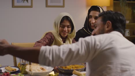 familia musulmana sentada alrededor de una mesa en casa con comida para comer celebrando eid posando para selfie 2