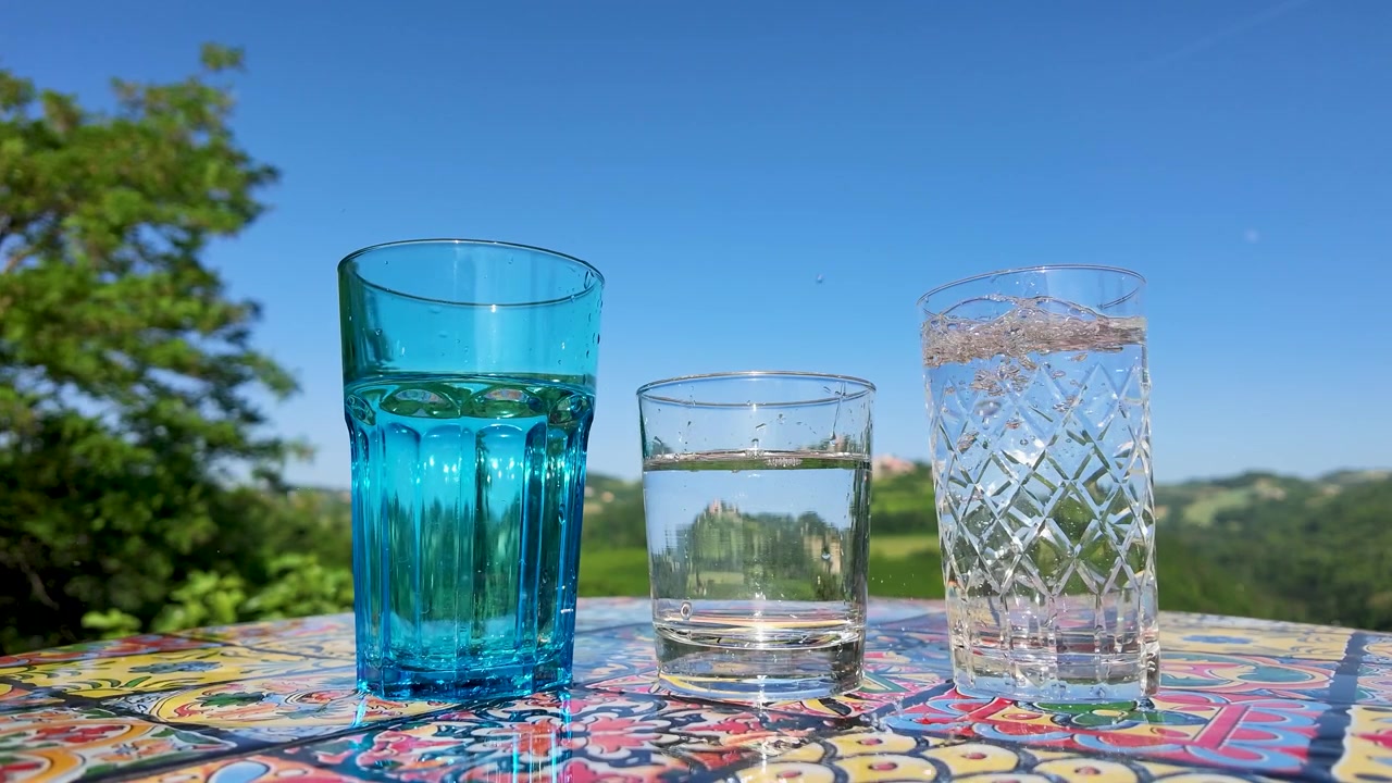 Acqua frizzante si versa in un bicchiere di cristallo su un tavolo piastrellato sotto un cielo sereno.
