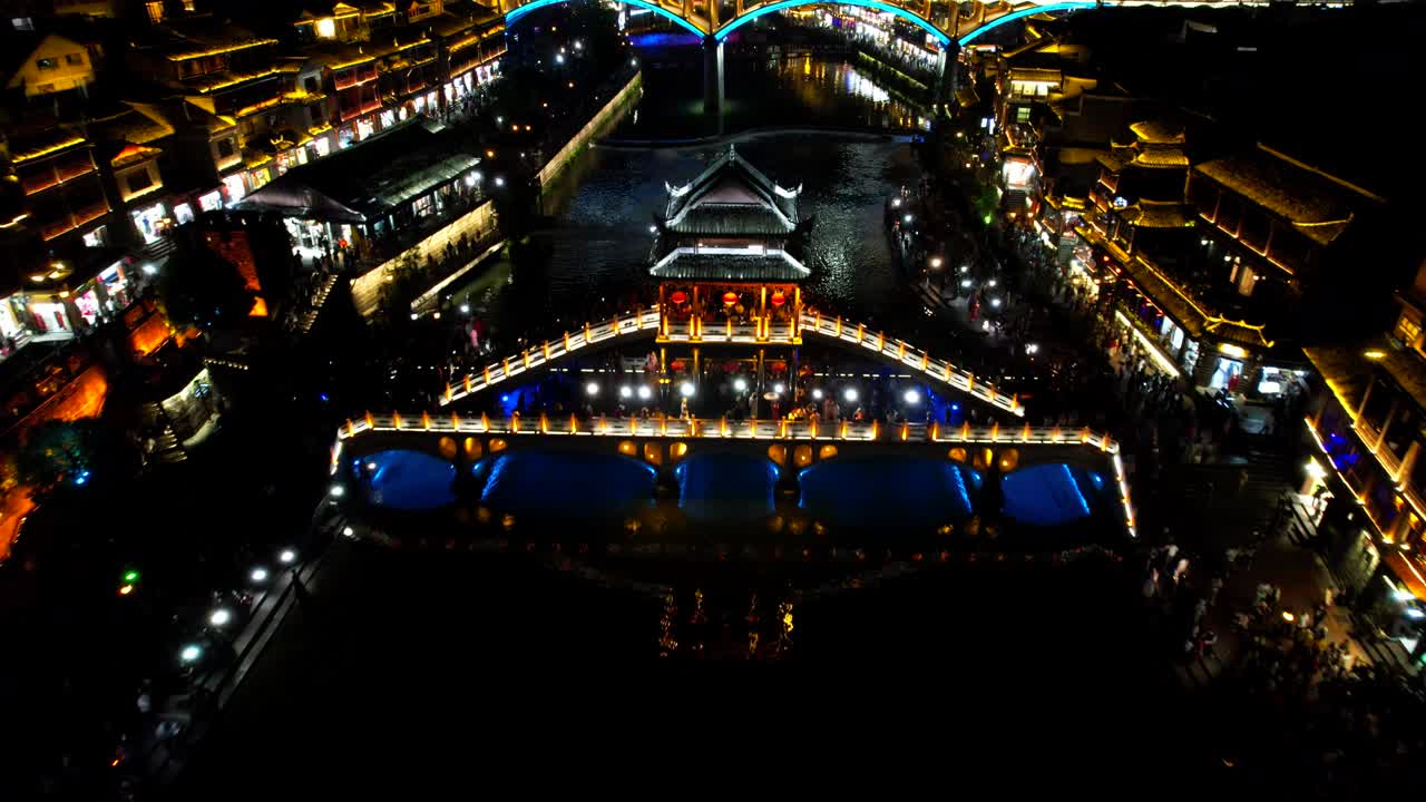 Aerial night reveal shot of illuminated Snow Bridge and Tuo Jiang, Fenghuang