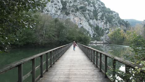 Serene-woman-in-outerwear-walking-on-footbridge-over-tranquil-lake