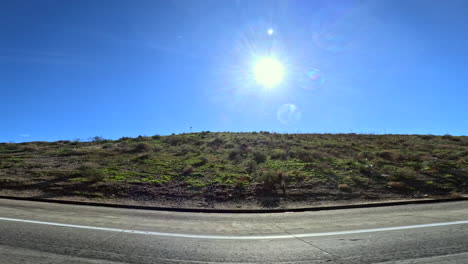 looking out the passenger window of a car on california state route 14 passing green rolling grassland hills