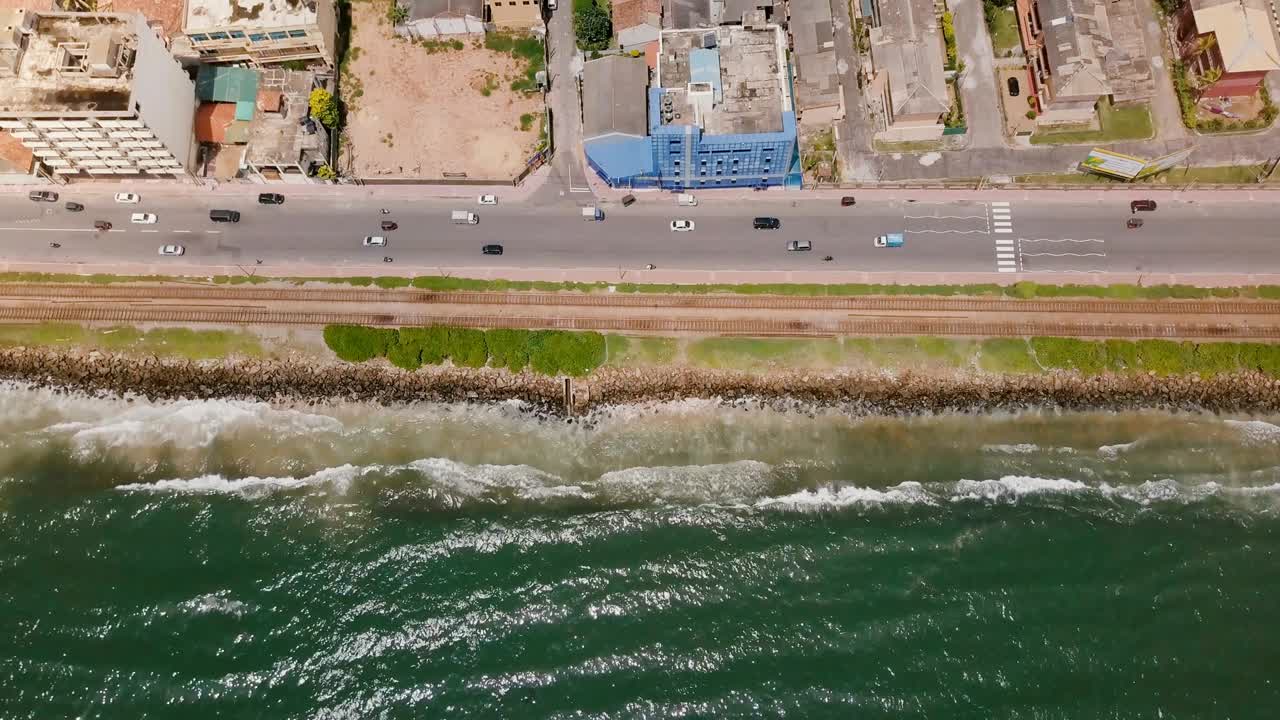 스리랑카의 콜롬보를 향해 해안선 위를 날아가는 드론. 바다의 파도, 거리 및 도시 건물의 위상.