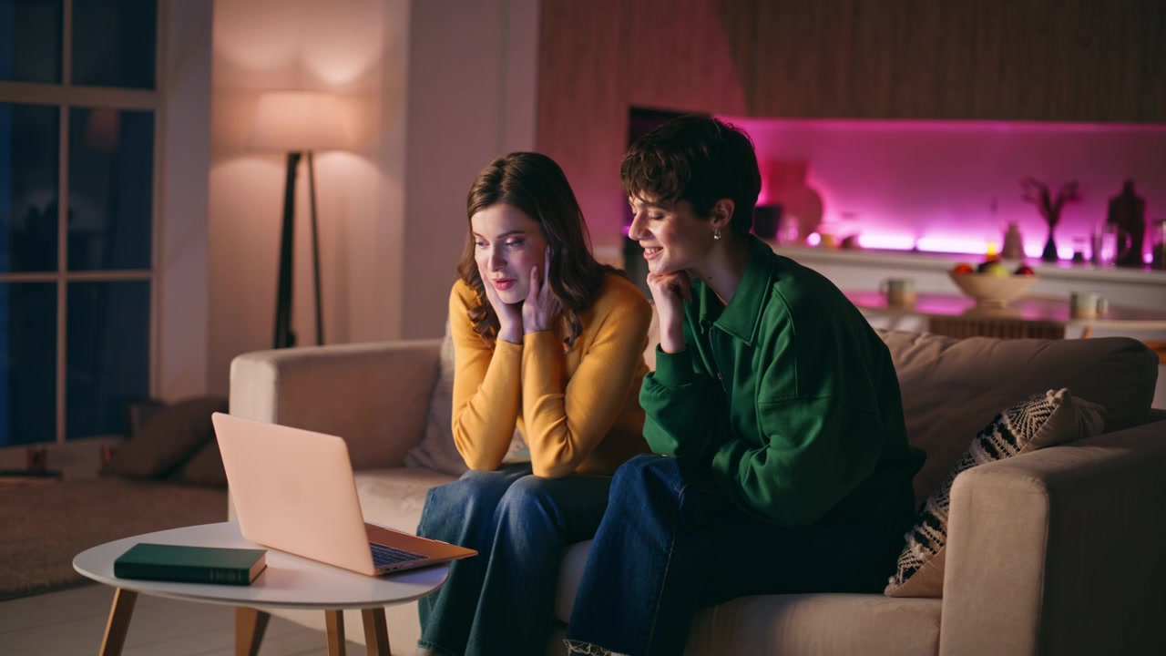 Two friends greeting laptop webcam sitting home couch. Couple online meeting