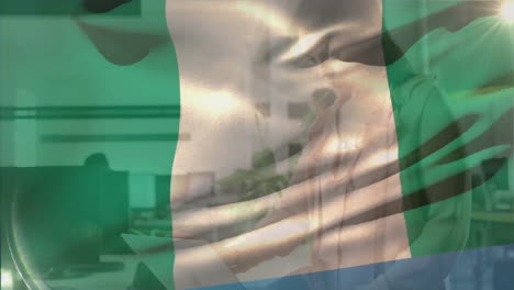 animation of flag of nigeria waving over caucasian businesswoman studying document at casual office