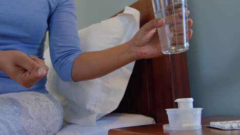 Front-view-of-mature-Caucasian-woman-taking-medicine-with-glass-of-water-in-a-comfortable-home-4k