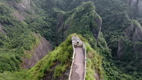 Woman-hiking-dramatic-mountain-peak-viewpoint,-Bajiao-Shan-China,-aerial-reveal