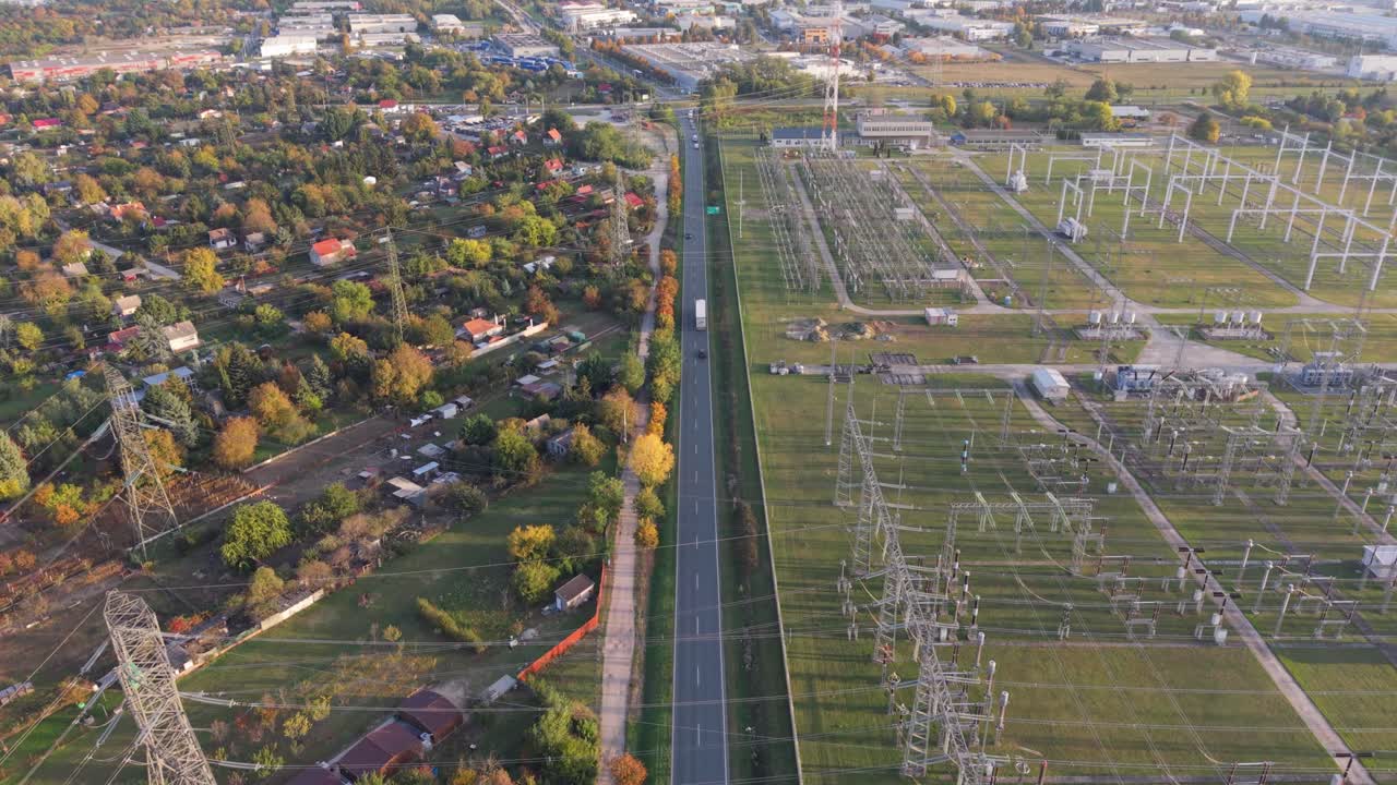 A drone aerial video showing a suburban area divided by a main road, with a large electrical power station on one side and residential houses on the other