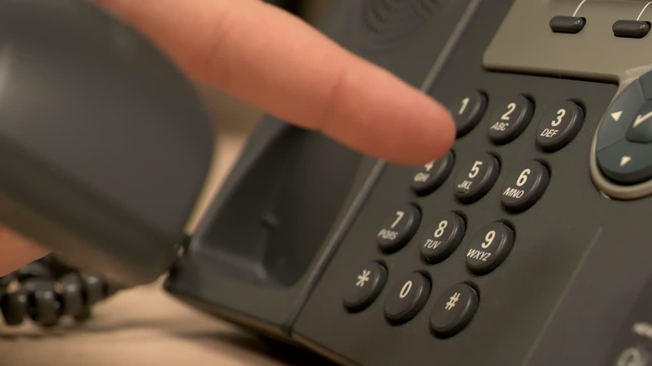 un primer plano de un teléfono de oficina de escritorio mientras una mano presiona botones, quita el receptor y lo vuelve a colocar en la base en cámara lenta