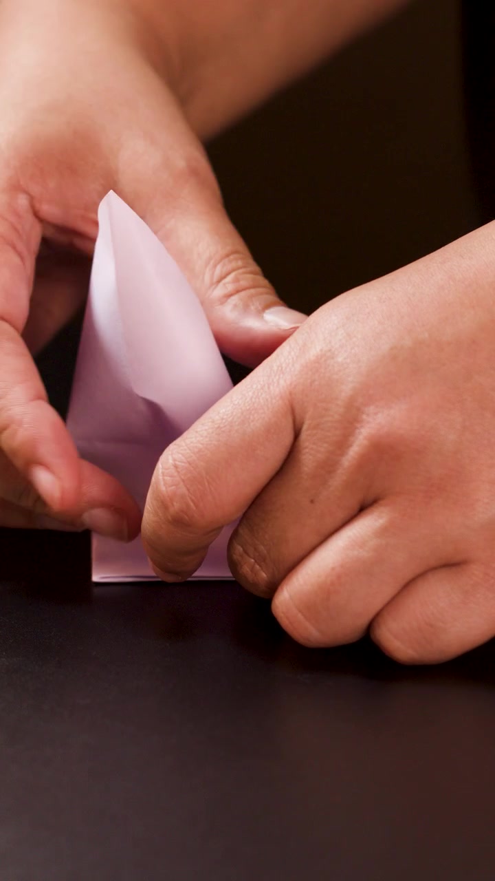 Adult hands carefully fold white paper into an origami boat under soft, even lighting