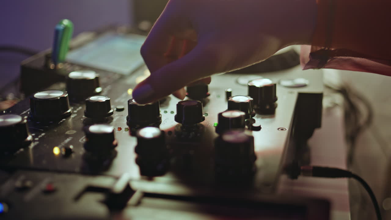 DJ hand tweaking knobs on mixer mixing music in clubbing scene closeup