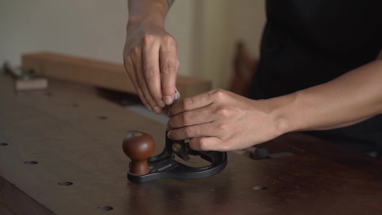 Close up of craftsman adjusting hand plane on workbench before planing timber, fine tuning blade for woodworking task in carpentry workshop during daytime