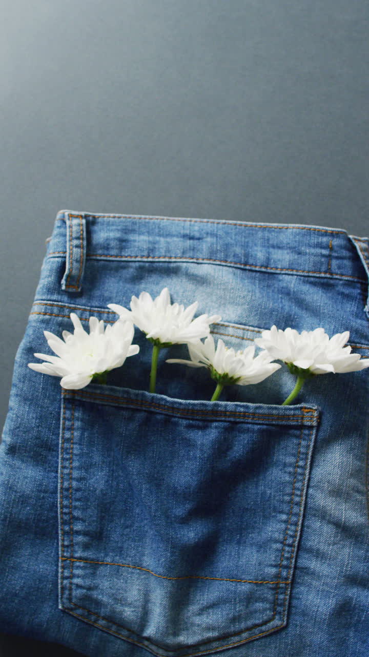 Vertical video of jeans with white flowers on grey background with copy space