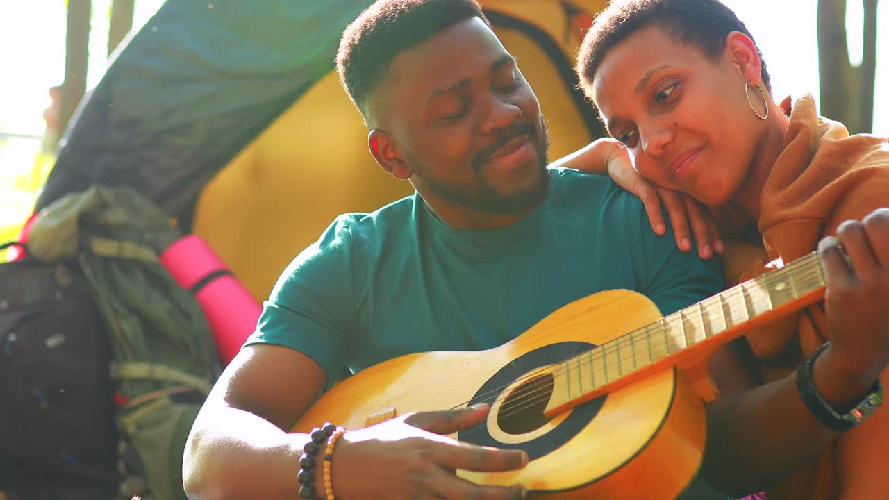 dos africanos americanos felices enamorados pasando tiempo al aire libre en el campamento tocando la guitarra y cantando