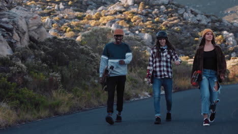 multi ethnic skater friends holding longboards hanging out together enjoying summer vacation longboarding walking on countryside road having conversation at sunset