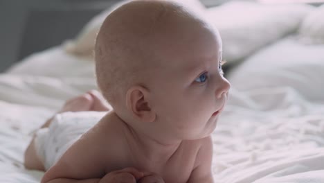 newborn baby lying on bed on front and looking around