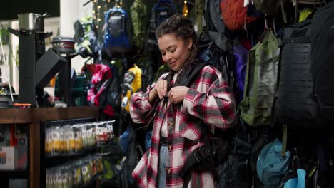Young-woman-trying-big-tourist-rucksack-in-sports-equipment-store
