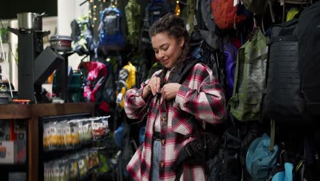 young woman trying big tourist rucksack in sports equipment store