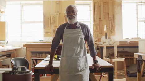 portrait of african american male carpenter wearing an apron standing in a carpentry shop