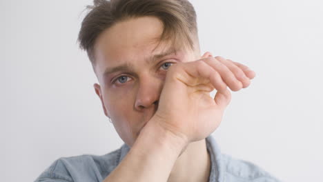 un hombre triste y guapo quitándose las gafas y limpiándose las lágrimas