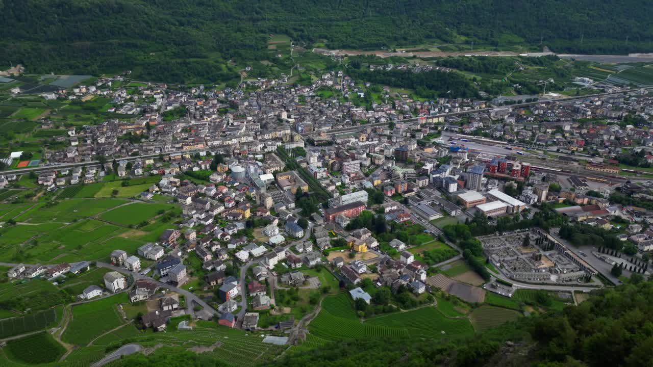 Detailed drone shot of Tirano’s urban sprawl with visible railway terminal, industrial buildings, green areas, and clustered housing. Aerial in Tirano, Italy Italia