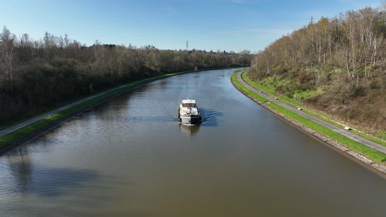 A boat advances calmly along a canal in Brussels, Belgium, surrounded by green banks and trees under clear skies