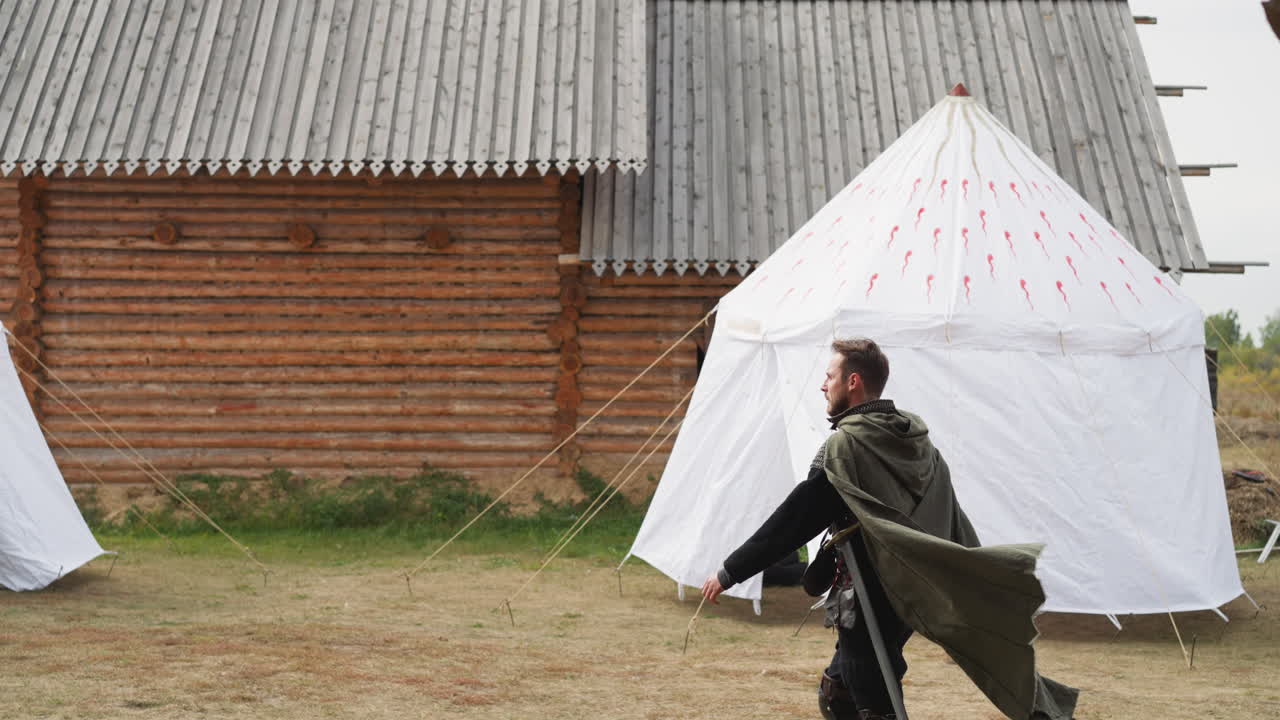 망토를 입은 숙련된 중세 전사가 정착촌을 가로질러  ⁇ 습니다.