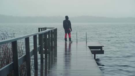 man walking on a wet pier and looking towards the lake on a cold and rainy day