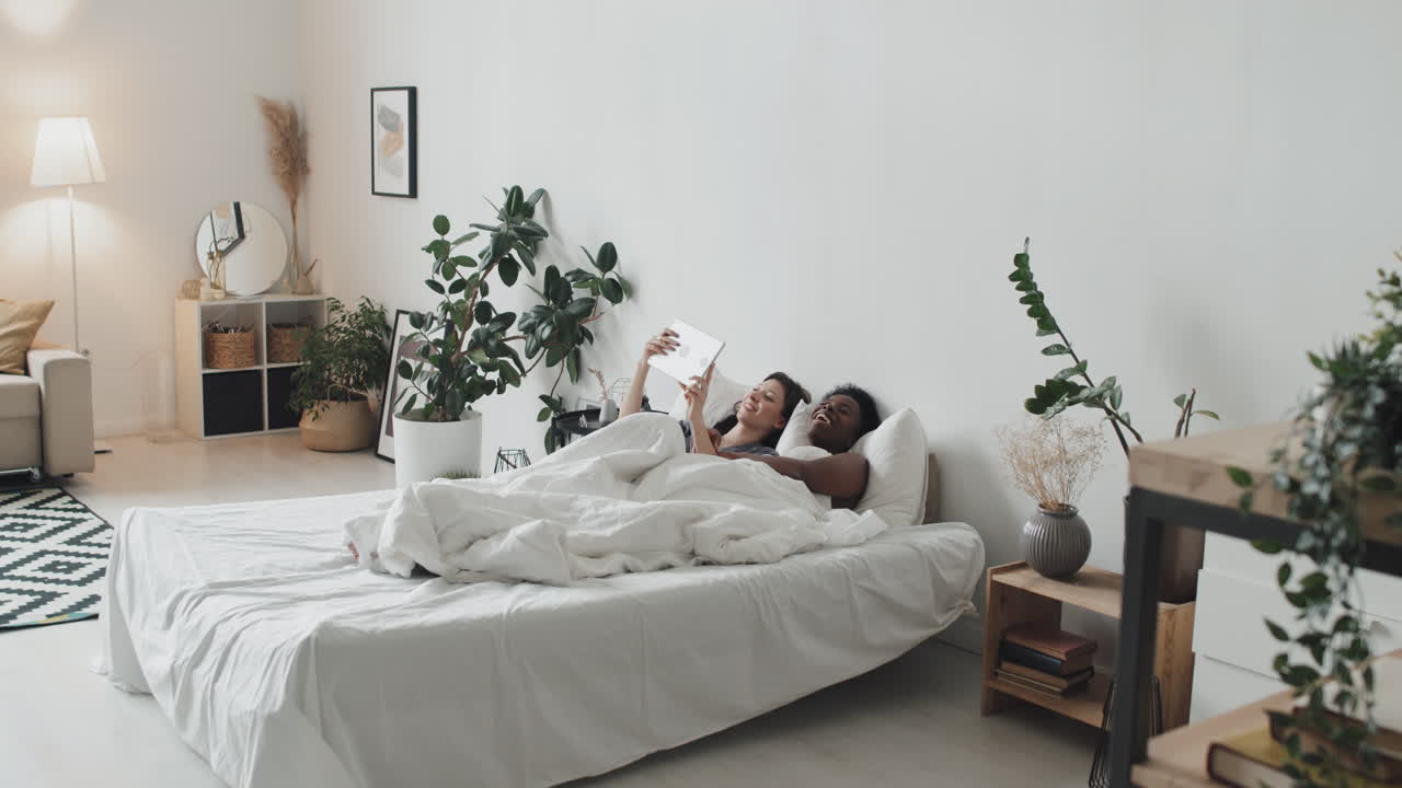 LGBTQ Couple with Tablet Lying in Bed in Cozy Apartment