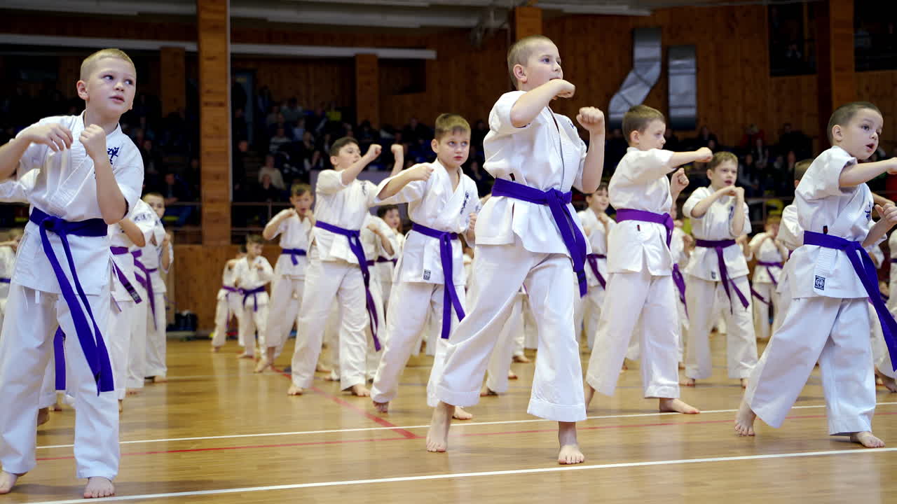 Young athletes in white kimonos practice punches with hands. Children working out the kicks in the big gym.