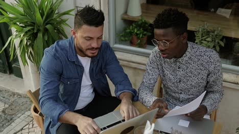 Young-freelancers-discussing-work-and-smiling-in-outdoor-cafe