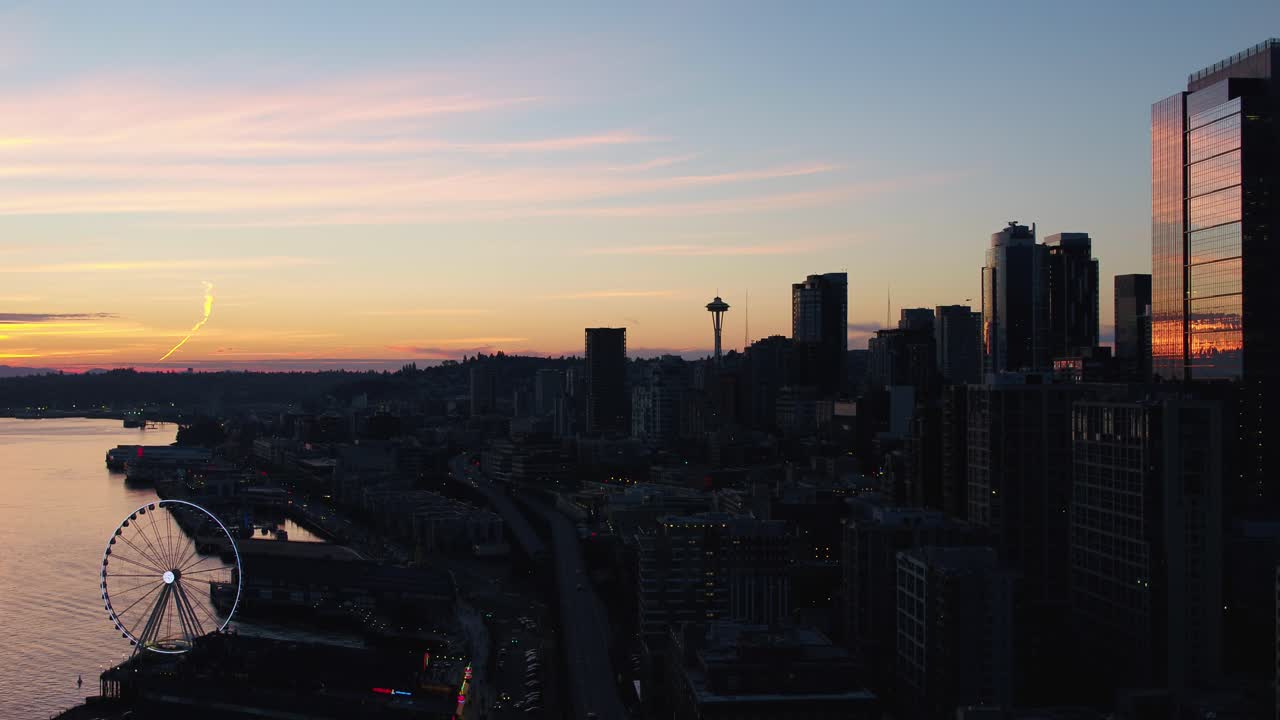 Aerial of Seattle's downtown corridor at sunset. Silhouettes of the big wheel and the Space Needle are easily visible.