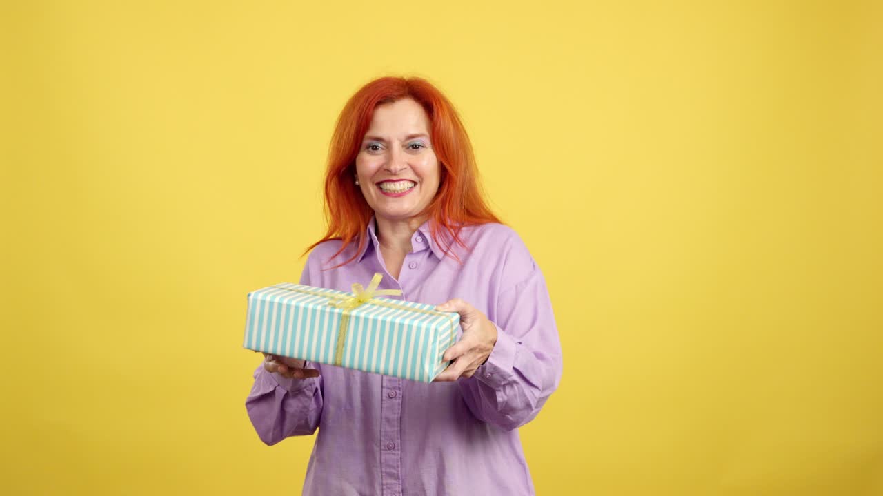 Happy woman with red hair offering a gift box on a yellow background
