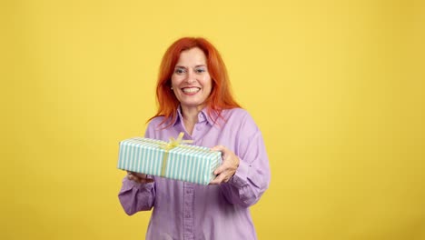 happy woman with red hair offering a gift box on a yellow background