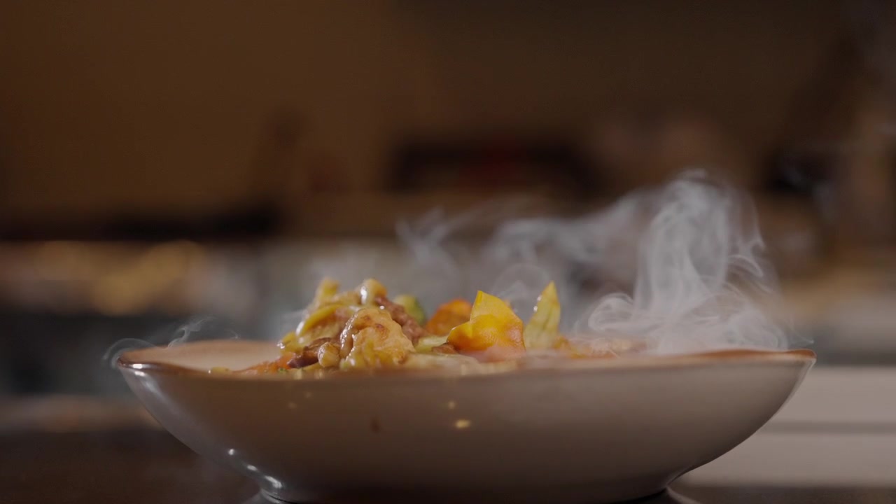 Close-up de prato quente com vapor subindo de comida recém-preparada em ambiente de restaurante.