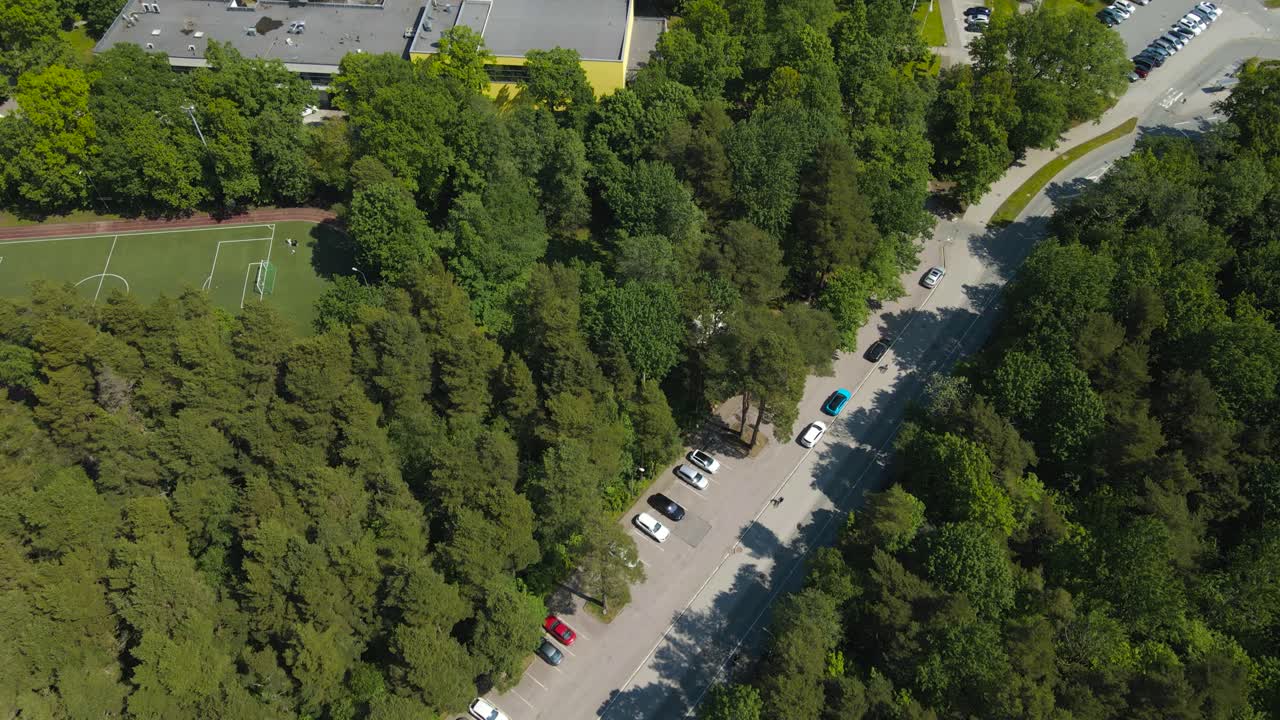 Gorgeous revealing aerial drone footage of a yellow colored modern school on Baltic sea shoreline during a summer sunny day, school has renewable energy solar panels on it and is in a green forest.