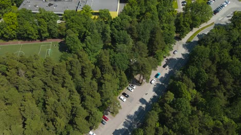 gorgeous revealing aerial drone footage of a yellow colored modern school on baltic sea shoreline during a summer sunny day, school has renewable energy solar panels on it and is in a green forest.