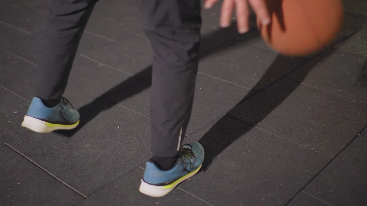 night street court feet dribbling, player practicing lowangle footwork on asphalt, blue sneakers tapping ball, long shadow cast by harsh lighting, slow rhythmic bounce, focused solo training, urban