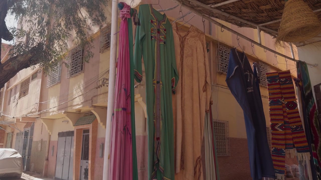 Colorful djellabas and striped woven blankets hanging outside a street market stall in a Moroccan medina