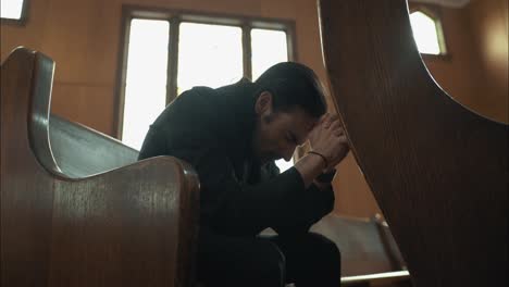 young man in black suit praying in church in cinematic slow motion