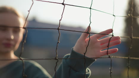 lady in green sweater gliding hand over volleyball net with sunlight reflecting off her face, focus on hand movement, blurred background of volleyball court with soft daylight