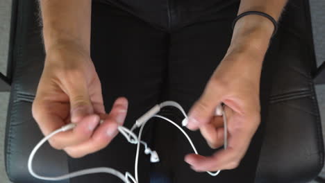 vista superior de las manos desenredando con éxito los auriculares blancos en la oreja