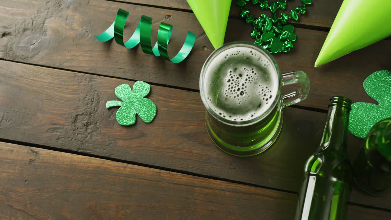 Video of st patrick's green beer, shamrock and bottle on wooden background