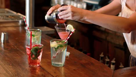 barmaid pouring cocktail in glass at bar counter