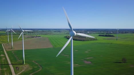 aerial view of wind turbines generating renewable energy in the wind farm, sunny spring day, low flyover over green agricultural cereal fields, countryside roads, drone dolly shot moving right