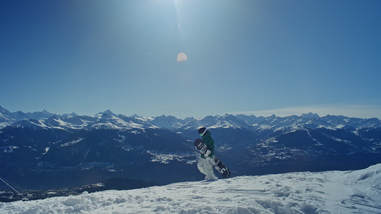 Uno snowboarder cammina lungo un crinale montano ad Anzère con viste spettacolari sulla Valle del Rodano e sulle Alpi Svizzere. Luce invernale limpida, vasto paesaggio alpino e un'atmosfera da avventura cinematografica.