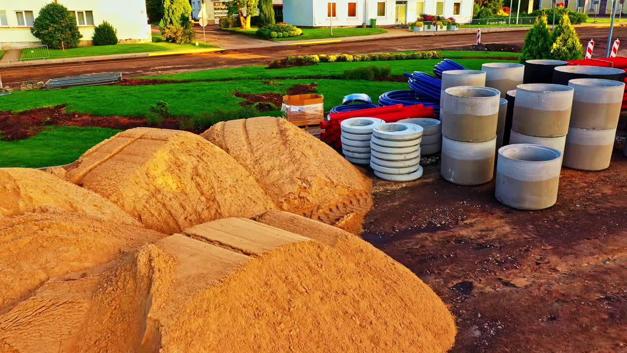 Construction sand piles and pipes in residential area with machinery and supplies